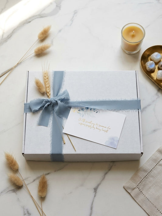 Gift box with a periwinkle ribbon on a marble surface with decorative elements.