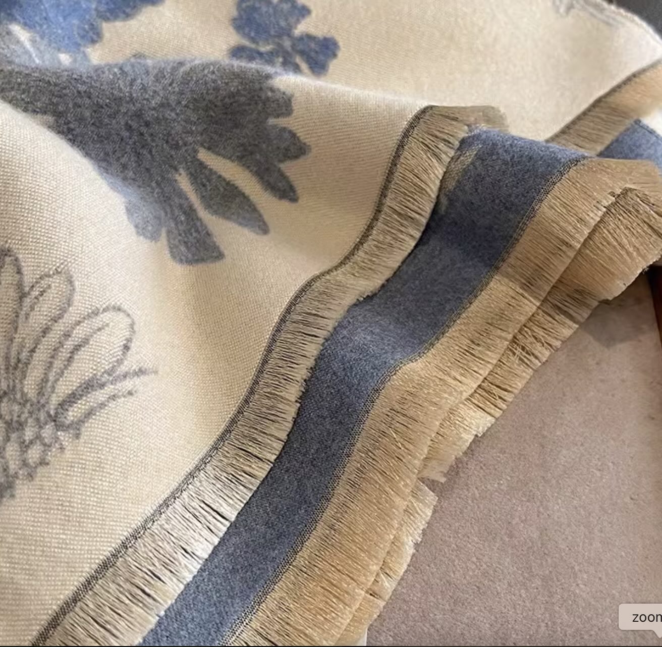 Close-up of a wool scarf with floral patterns and fringes.