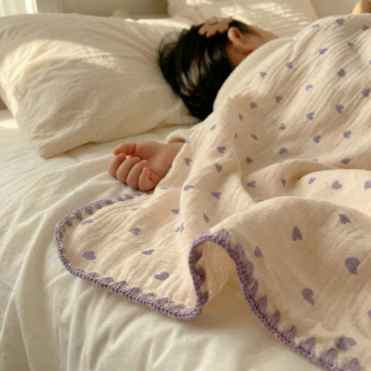 Cloud cotton muslin blanket in Lavender Hearts draped on bed — purple hearts on cream, MonBebe Singapore
