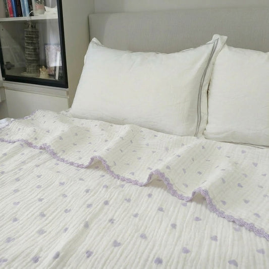 Cloud cotton muslin blanket in Lavender Hearts draped on bed — purple hearts on cream, MonBebe Singapore