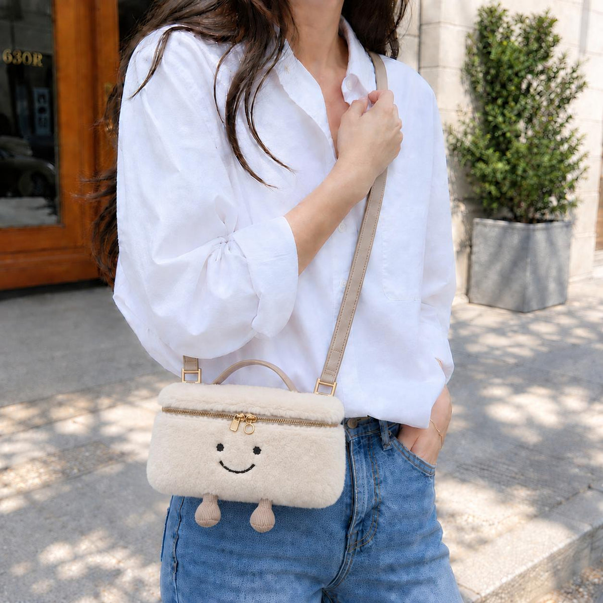 Woman wearing cream furry Laura Smiley crossbody bag over white shirt and jeans, outdoors