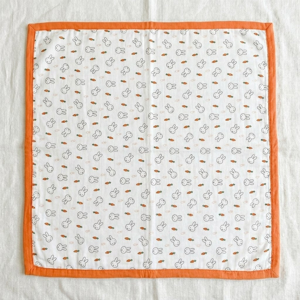 Tokki four-layer bamboo cotton blanket laid flat showing full bunny and carrot print with orange border, MonBebe